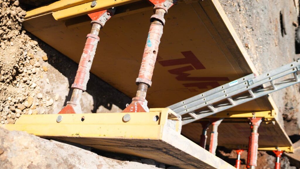 Bauarbeiter sichert einen tiefen Graben mit einem Verbau-System und Klemmen im Tiefbau.