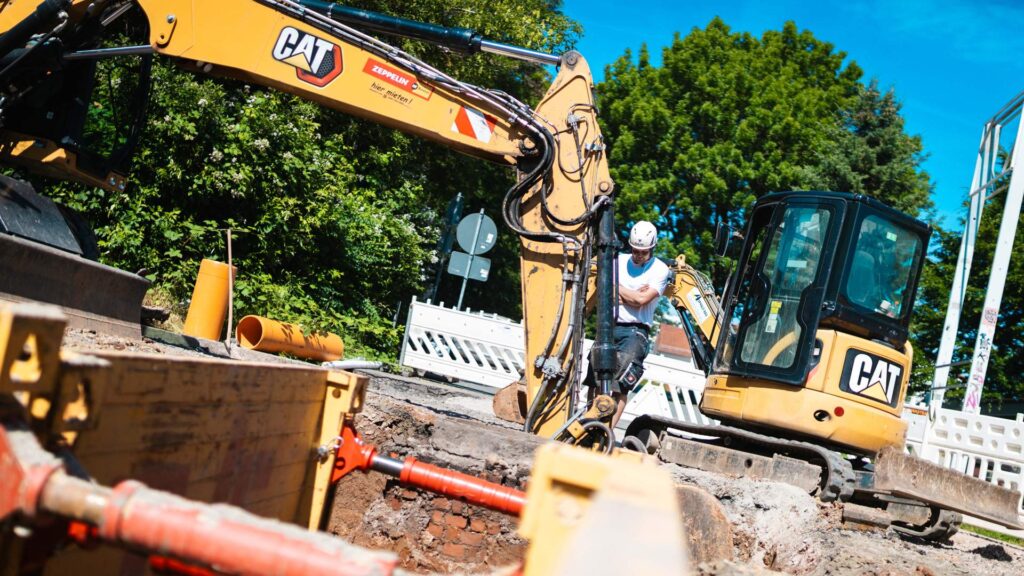CAT-Bagger arbeitet auf einer Straßenbaustelle zur Erneuerung von Infrastruktur und Rohren.