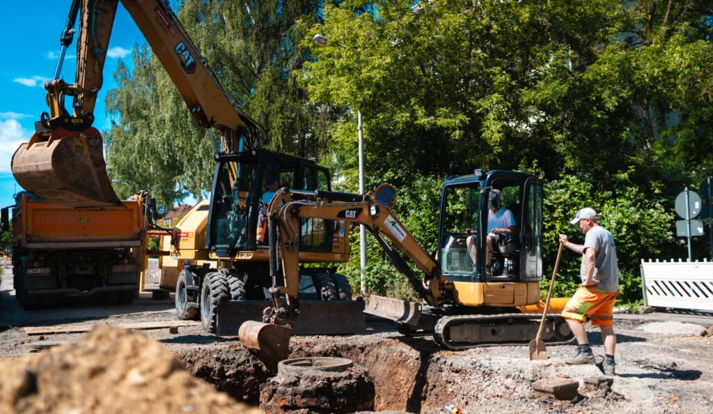 Mehrere Bagger und Straßenbauarbeiter sichern die Baustelle für Rohrverlegearbeiten.