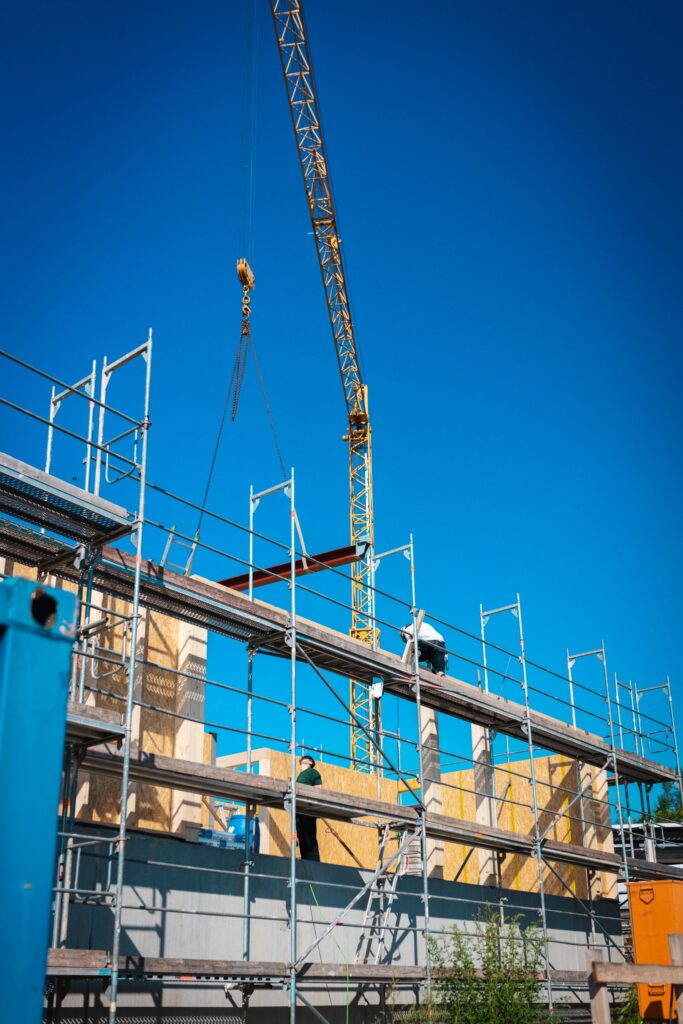 Turmdrehkran hebt Stahlträger über Gerüst und Holzbau-Rohbau