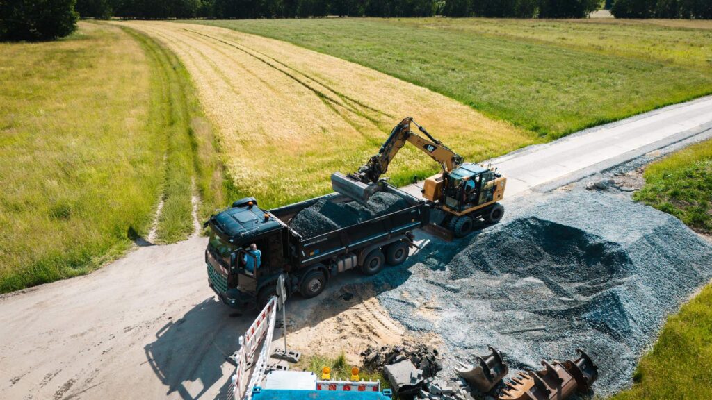 Drohnenaufnahme: CAT-Mobilbagger belädt einen Lkw auf einer Landstraßenbaustelle