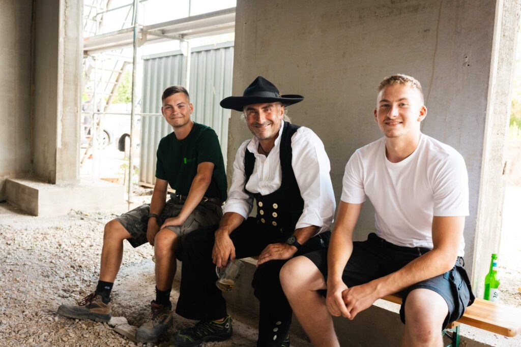 Zimmerer in traditioneller Kluft sitzt zusammen mit Handwerkern im Rohbau auf der Baustelle beim Richtfest in St. Egidien.