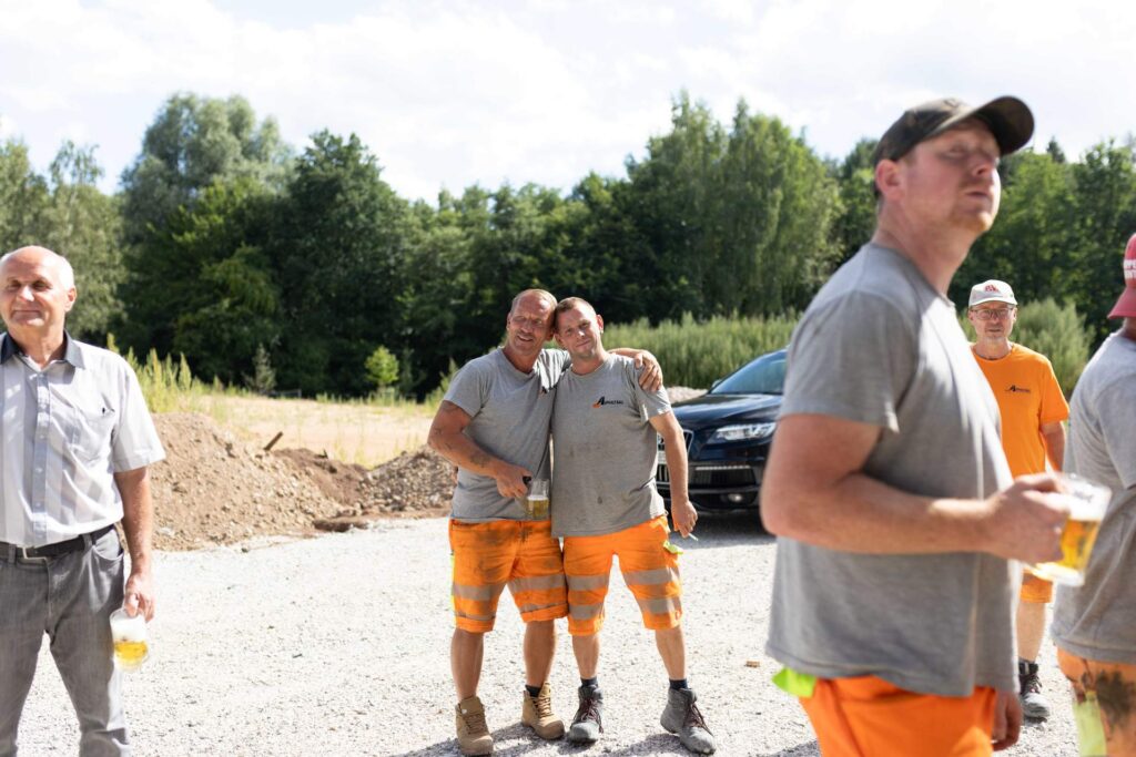 Zwei Bauarbeiter von Asphalt-Bau Chemnitz umarmen sich lächelnd beim Richtfest auf der Baustelle.